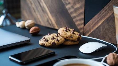 Image of a desktop setup with a laptop, smartphone, mouse, keyboard, and cookies on a plate